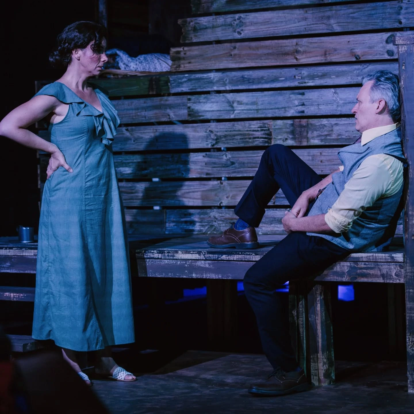 Josie stands over Tyrone, who sits on the farmhouse steps under blue light, in 'A Moon for the Misbegotten' at ABET.