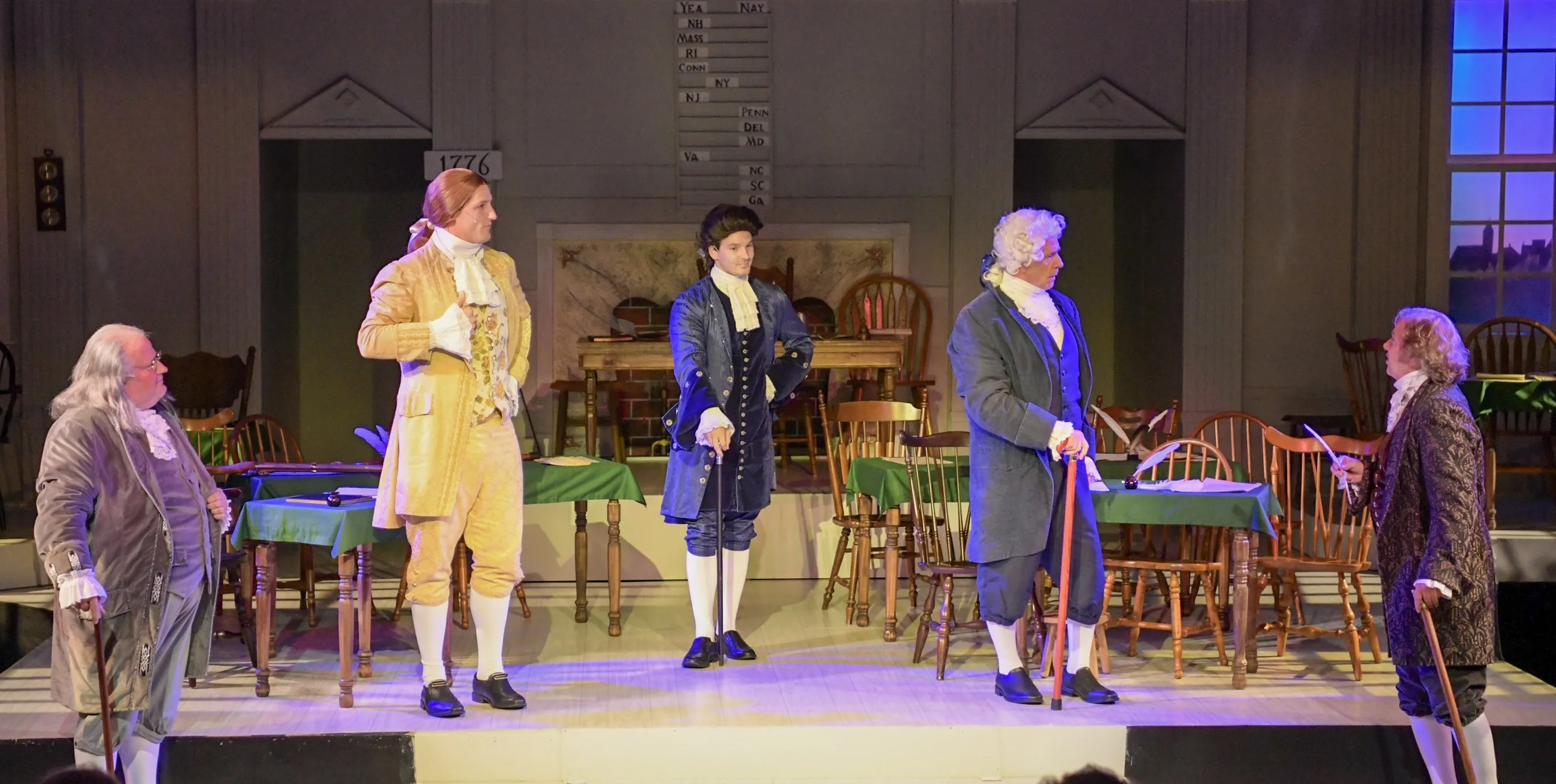 Five actors in 18th-century colonial dress — playing Franklin, Jefferson, Livingston, Sherman and Adams of the Declaration Committee — stand in a line on the Continental Congress chamber set in Alhambra Theatre & Dining's 1776, with the YEA/NAY state tally board visible upstage.